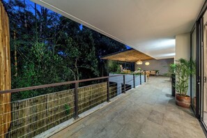 A modern outdoor balcony with a view of dense trees, a wooden fence, and a seating area with a table and chairs. - Hidden 3BR Ubud Oasis w Pool & Open-Plan Living (Gianyar Regency)