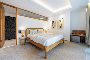 A modern bedroom with a wooden bed, a stone wall, and a small desk with a lamp. - Hidden 3BR Ubud Oasis w Pool & Open-Plan Living (Gianyar Regency)