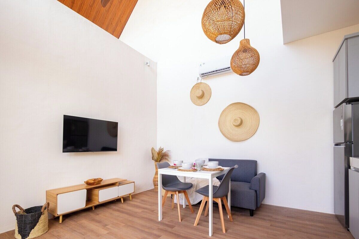 A modern living space with a flat-screen TV, a dining table with chairs, a sofa, and a kitchen area with a refrigerator.