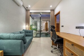 A modern interior with a sofa, desk, and glass doors leading to a pool area. - Peaceful 1BR Retreat w Pool in Prime Seminyak (Kota Denpasar)