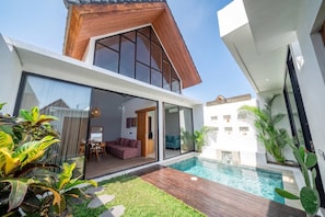 A modern house with a glass-enclosed living area, a wooden deck, and a swimming pool. - Peaceful 1BR Retreat w Pool in Prime Seminyak (Kota Denpasar)