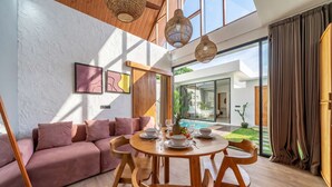 Un salon moderne avec une table de salle à manger ronde en bois, un canapé rose et une vue sur une piscine.
