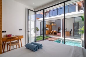 Et moderne soveværelse med en stor seng, et skrivebord og udsigt til en swimmingpool og et køkken.