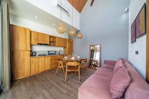 A modern kitchen with wooden cabinets and a dining area with a pink sofa. - Peaceful 1BR Retreat w Pool in Prime Seminyak (Kota Denpasar)