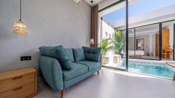 Una sala de estar moderna con un sofá color turquesa, una mesita de madera y un ventanal de vidrio que da a una zona de piscina.