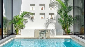Un espace piscine agrémenté d’un mur blanc orné de plusieurs vases et d’une petite cascade.