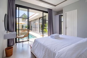 Ein modernes Hotelzimmer mit einem großen Bett, Blick auf einen Swimmingpool und einem Balkon mit Gartenmöbeln.