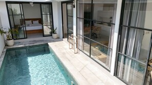 En modern inredning med en swimmingpool, en säng med ett träfärgat huvudgavel och en matplats med möbler i rotting.