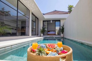 Ein moderner Poolbereich mit Essplatz, ausgestattet mit einer Obstschale und zwei Gläsern Orangensaft.