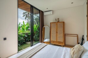 A bedroom with a large window, a bed, a wardrobe, and an air conditioning unit. - 3BR Villa in Jungle Ubud • Private Pool & Patio (Gianyar Regency)