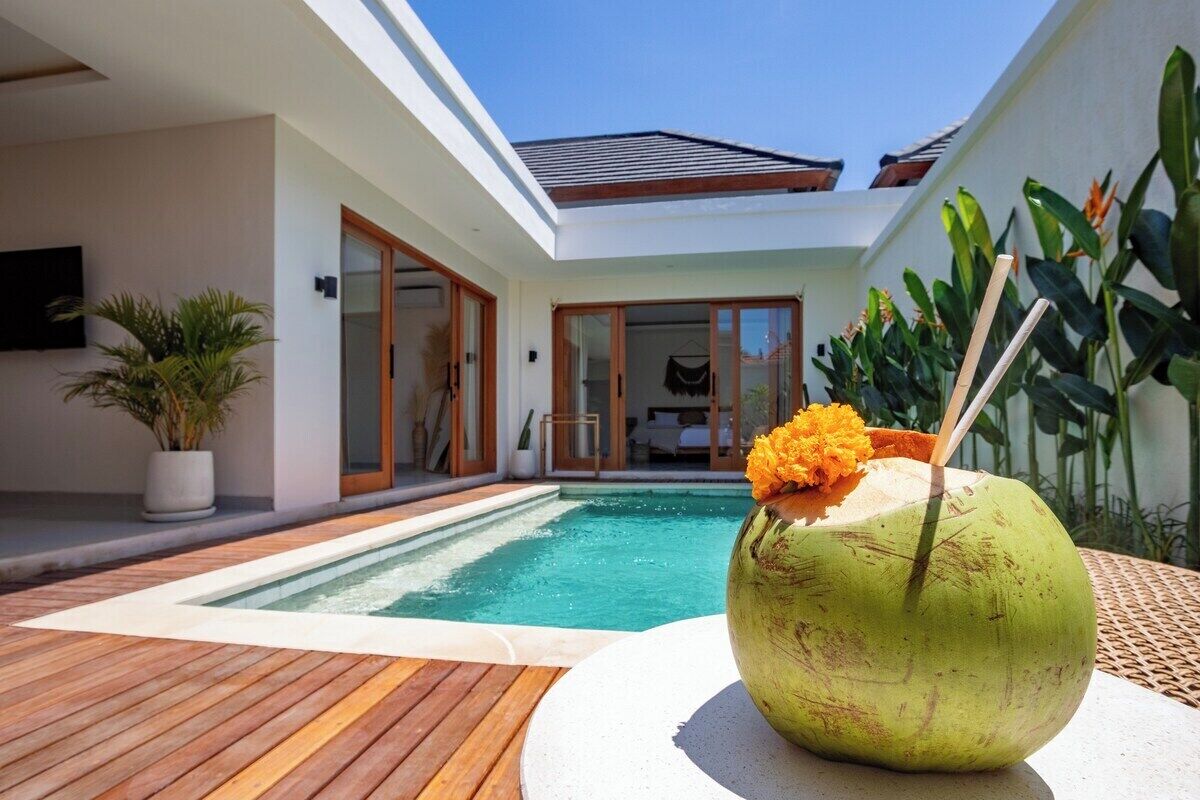 Ein modernes Haus mit Swimmingpool, einer Holzterrasse und einem Kokosdrink mit einer Blume auf einem Tisch.