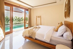 A bedroom with a bed, a wooden headboard, a view of a pool, and a sliding glass door. - Serene Retreat Villa in Canggu Perfect for Strolls (Kabupaten Badung)