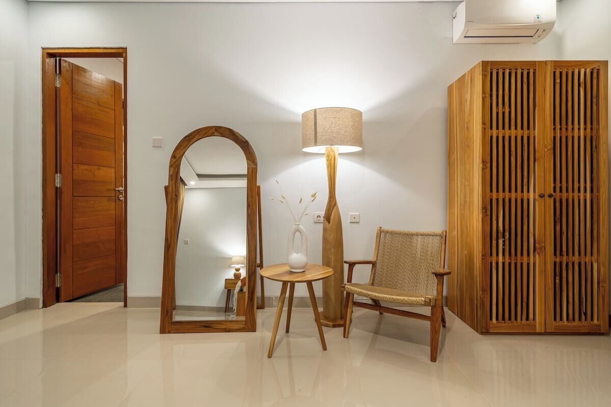A room with a wooden door, a mirror, a lamp, a chair, and a wardrobe.