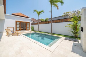 Ein Pool mit Liegestühlen, ein Holzzaun und eine weiße Wand mit einer Tür zu einem Raum.