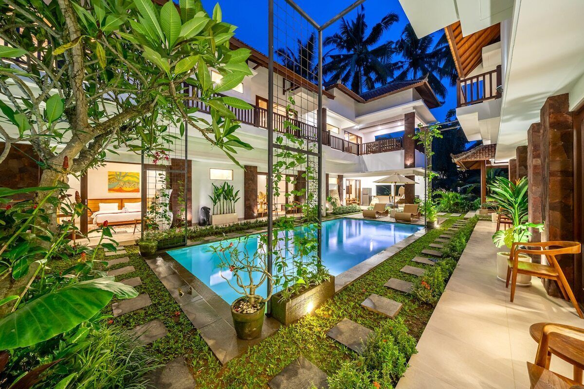 A modern multi-story building with a swimming pool, outdoor seating, and lush greenery.