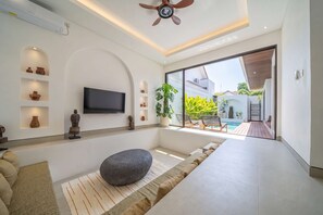 Un salon moderne doté d’un téléviseur à écran plat, d’un banc en pierre et offrant une vue sur une piscine et la verdure environnante.