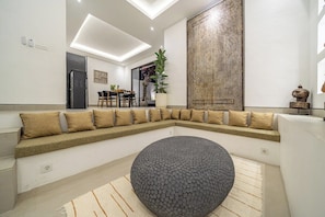 Un salon moderne avec un canapé d’angle, un pouf rond et un grand élément décoratif mural.