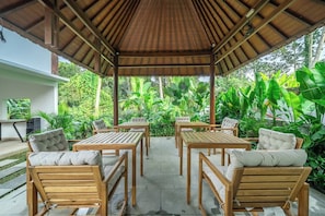 An outdoor covered patio with wooden tables and chairs, surrounded by lush greenery. - Cozy 1BR w Spacious Pool+Garden • Ubud's Best Spot (Gianyar Regency)