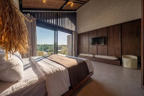 Ein modernes Schlafzimmer mit einem großen Bett, einem an der Wand montierten Fernseher und Blick ins Freie.