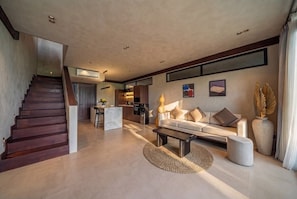 Ein modernes Wohnzimmer mit Treppe, einer Sofagarnitur und einer Küchenzeile.