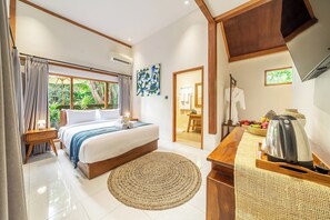 A bedroom with a bed, a bedside table, a coffee table, a TV, and a view of the outdoors. - Serene Ubud 1BR w Pool & Lush Garden, Top Location (Ubud)