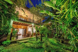 Ein zweistöckiges Gebäude mit Balkon, umgeben von üppiger Vegetation und einem kleinen Teich.