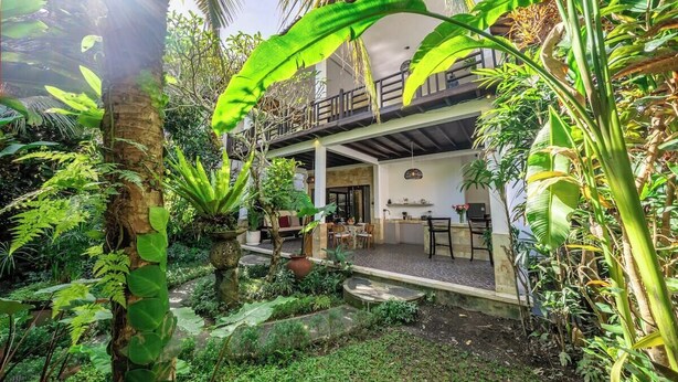 Un bâtiment à deux étages doté d’un balcon, entouré d’une végétation luxuriante et d’un jardin.