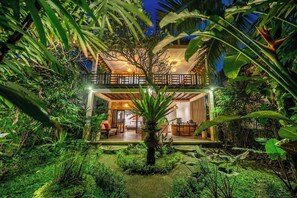 Un bâtiment à deux étages doté d’un balcon, entouré d’une végétation luxuriante.