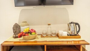 Ein Holztisch mit Obstschale, Dekoration, Gläsern, einem Wasserkocher und einem darüber montierten Fernseher.