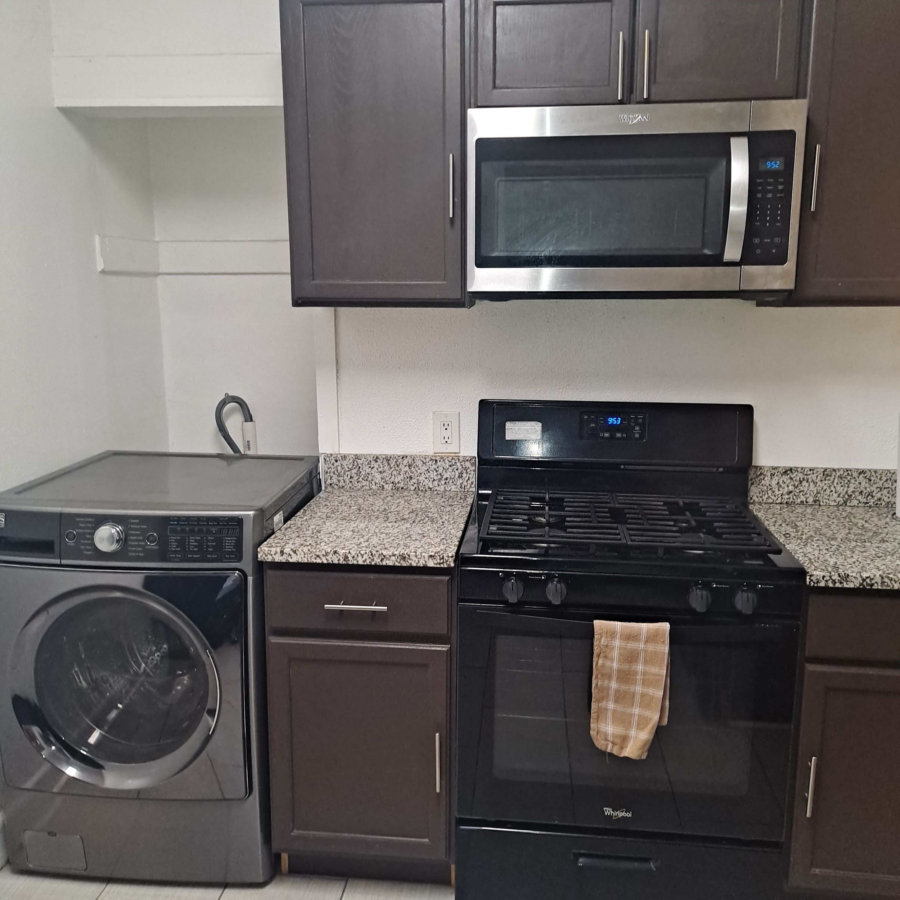 Una cocina con un microondas de acero inoxidable, una estufa Whirlpool negra y una lavadora de carga frontal.