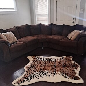 A living room with a brown sectional sofa, a white door, and a large animal hide rug. - Lovely 2-bedroom apartment with AC in vibrant Cleveland (Cleveland)