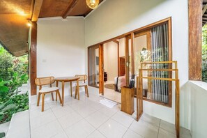 A room with a wooden table and chairs, a sliding glass door leading to a balcony, and a view of greenery outside. - Cozy 1BR Stay w Pool, Garden & Patio, Central Ubud (Kabupaten Gianyar)