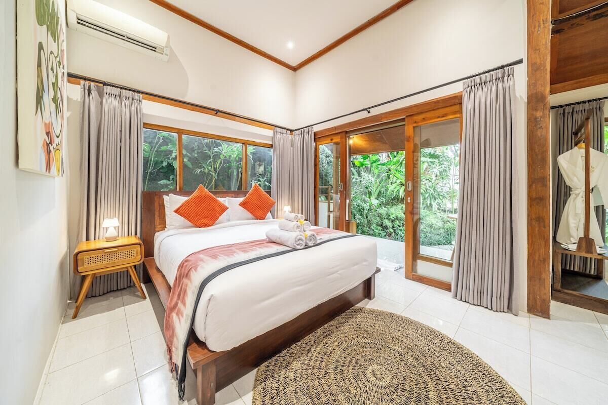 Een slaapkamer met een groot bed, een nachtkastje, een raam met gordijnen en uitzicht op groen.