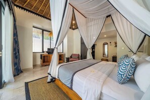 A spacious bedroom with a canopy bed, a wooden nightstand, a television, and a seating area with a chair and a small table. - Peaceful 1BR Retreat - Best Ubud's Place w Pool (Gianyar Regency)