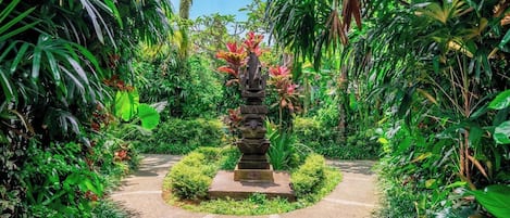 A garden pathway leading to a stone structure surrounded by lush tropical vegetation.