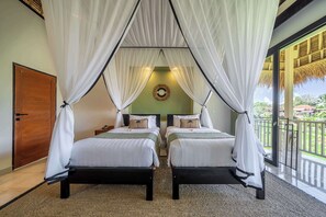 A double room with two beds, each with a canopy, a wooden door, a round mirror, and a view of the outdoors.