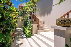 A staircase leading up to a building with a thatched roof, surrounded by lush greenery and a clear sky.