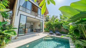 A modern two-story house with a glass-enclosed balcony, a swimming pool, and lush tropical plants. - New Tropical Villa+Large Pool+Perfect for Couples (Gianyar Regency)