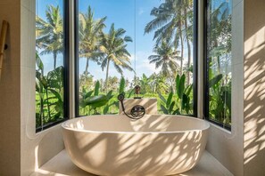 A modern bathroom with a freestanding bathtub, large windows, and a view of palm trees. - New Tropical Villa+Large Pool+Perfect for Couples (Gianyar Regency)