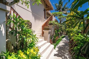 A staircase leading to a building with a thatched roof, surrounded by lush greenery and tropical plants. - Chic Grand Suite in Mesari Hotel - Lush Ubud (Gianyar Regency)