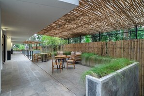 Een terras buiten met bamboevloer, houten meubilair en een betonnen plantenbak met gras.