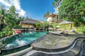 A swimming pool with lounge chairs and a thatched-roof structure. - Boho Grand Suite in Mesari Hotel Ubud (Gianyar Regency)