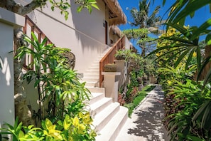 A staircase leading to a building with a thatched roof, surrounded by lush greenery and tropical plants. - Boho Grand Suite in Mesari Hotel Ubud (Gianyar Regency)
