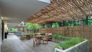 A covered outdoor seating area with tables and chairs, a bamboo fence, and a planter with grass. - New private apartments in Ubud, best location (Gianyar Regency)