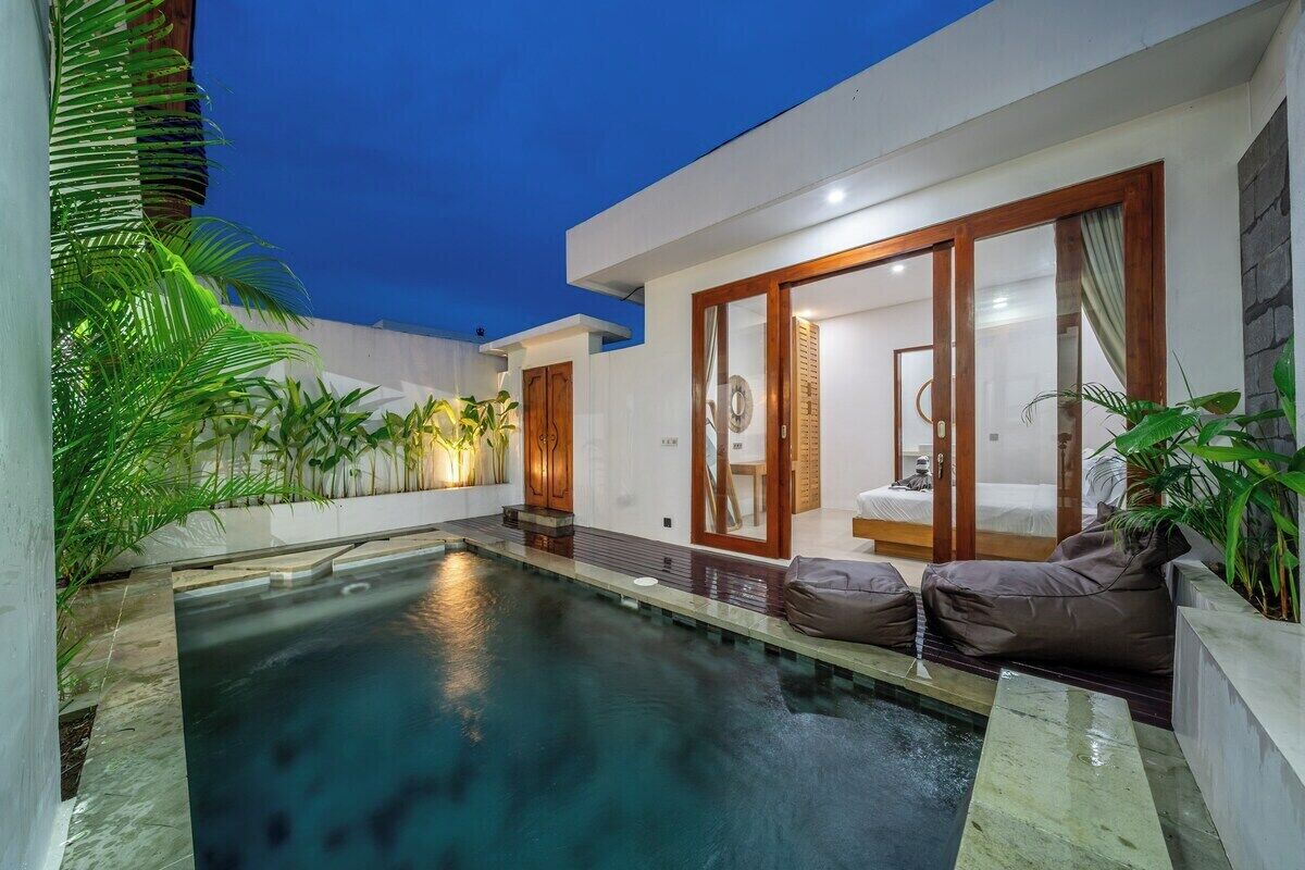A modern outdoor pool area with a glass-enclosed bedroom, surrounded by lush greenery.