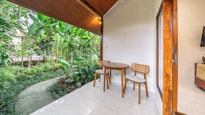 Un patio con mesa y sillas, rodeado de exuberante follaje y vistas a un jardín.