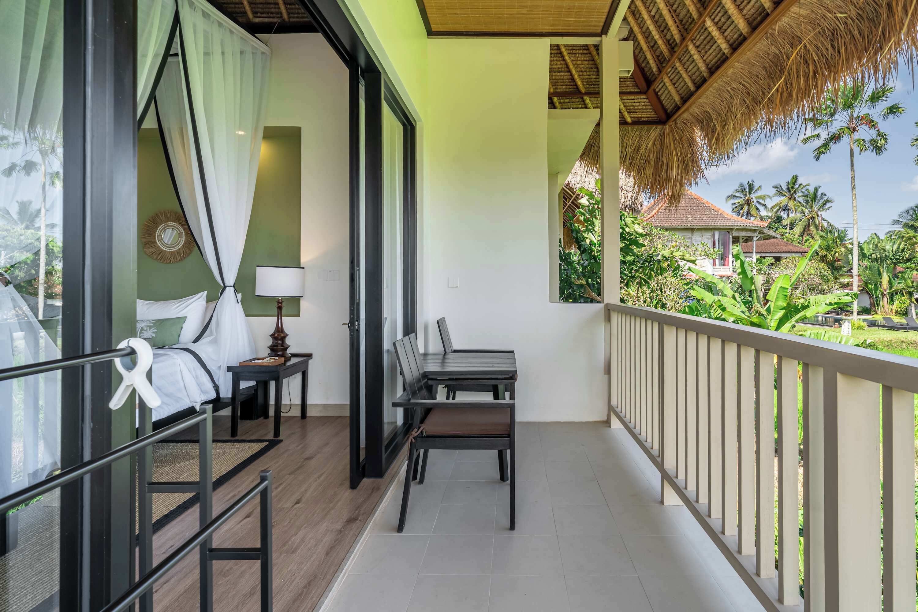 Un balcón con mesa y sillas, una cama con dosel y vistas a un paisaje tropical.
