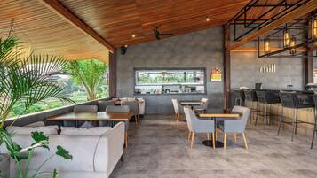 Un café moderne avec un plafond en bois, un espace salon avec des tables et des chaises, un bar avec des tabourets et une vue sur l’extérieur.