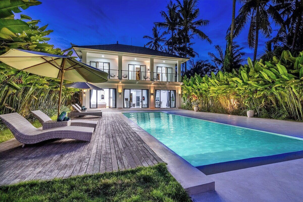 A two-story house with a swimming pool, surrounded by tropical vegetation.