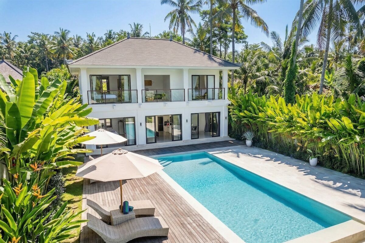 Ein zweistöckiges Haus mit Swimmingpool, umgeben von tropischer Vegetation.